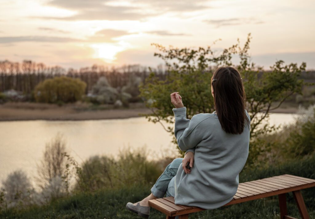 Terapia Psicológica para Adultos. Una mujer sentada en un banco mirando en el fondo la naturaleza