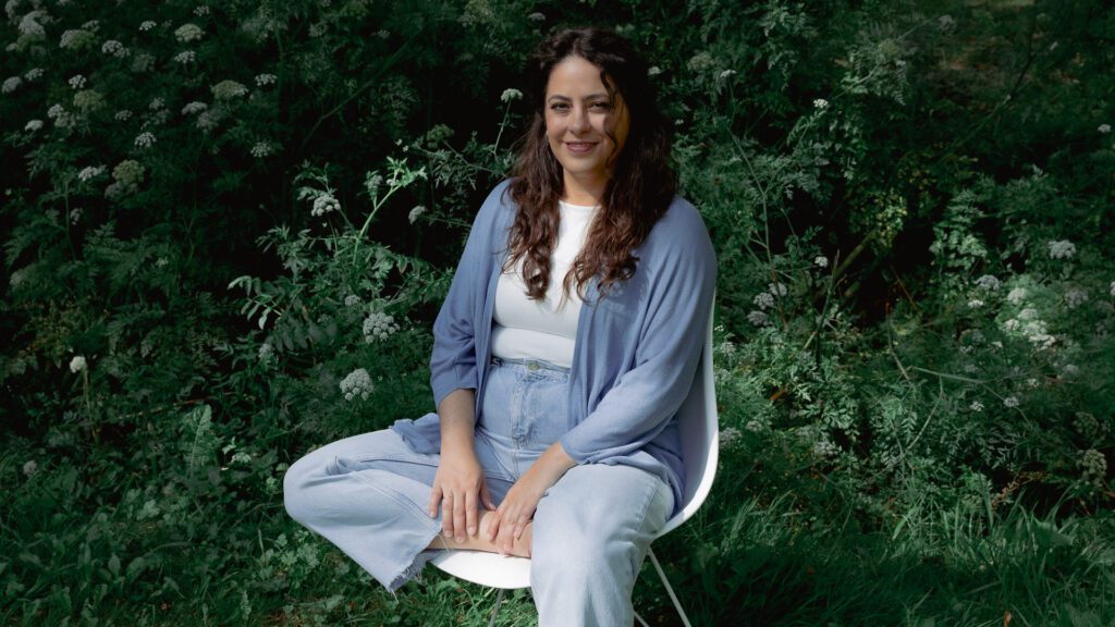 Andrea Guitérrez Psicoterapeuta sentada en una silla en un bosque entre flores